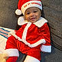 baby, child, smiling, christmas, holiday, santa_hat, red_clothing, white_fur_trim, couch, indoor, festive, cute, portrait, happy, holiday_season, young_child, face, sitting, sock, cozy