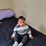 toddler, child, baby, bed, pillow, clothing, hoodie, pants, socks, hair, braids, face, skin, indoor, room, wall, curious, sitting, young, person