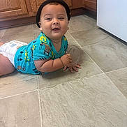 Xain joined the competition — help win amazing prizes! baby, child, infant, smiling, happy, portrait, indoor, kitchen, floor, tile, cabinet, appliance, dinosaur_clothing, blue_shirt, diaper, crawling, sitting, container, black_hat, home