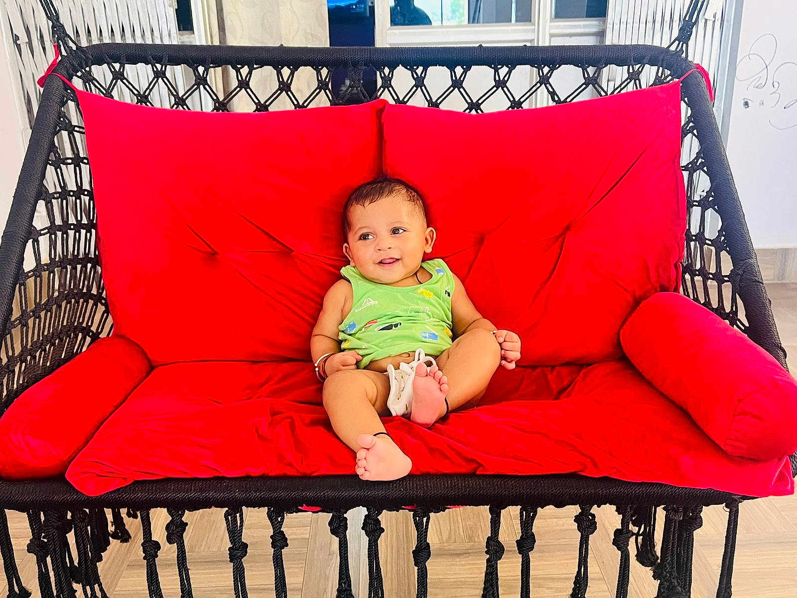 Avyan joined the competition — help win amazing prizes! baby, child, smiling, green_clothing, red_cushion, swing_chair, indoor, happy, feet, cushion, furniture, playful, person, infant, relaxing, seat, home, cute, smile, comfort