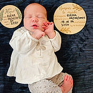 Eléna a rejoint le concours — aidez-le/la à gagner de superbes lots ! newborn, baby, infant, sleeping, clothing, blanket, plaque, wood, text, face, hand, foot, patterned_pants, white_shirt, portrait, laying_down, cute, peaceful, indoors, baby_photo