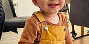 Raphael a rejoint le concours — aidez-le/la à gagner de superbes lots ! toddler, child, smiling, indoor, overalls, yellow_clothing, brown_clothing, face, happy, furniture, chair, table, floor, person, curly_hair, cute, standing, playful, young_child, expression