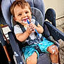 toddler, child, high_chair, blue_shorts, white_cream, spoon, smiling, messy, happy, face, hands, clothing, footwear, straps, seat, outdoor, concrete_floor, wall, baby_shoes, playful