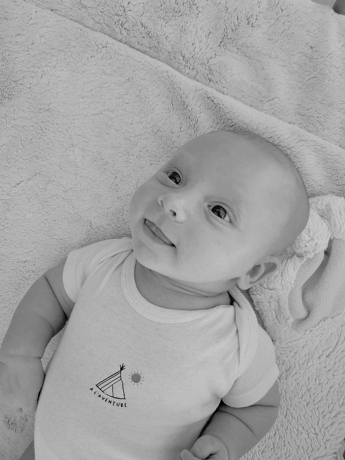 Nino a rejoint le concours — aidez-le/la à gagner de superbes lots ! baby, infant, onesie, blanket, cute, face, expression, child, smiling, tongue_out, sleepwear, soft_texture, portrait, lying_down, monochrome, black_and_white, young, head, hand, looking_up