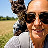 adventure, animal, backpack, blue_sky, casual_clothing, cat, close_up, daylight, field, happy, kitten, nature, outdoor, pet, portrait, shoulder, smile, sunglasses, sunny, woman