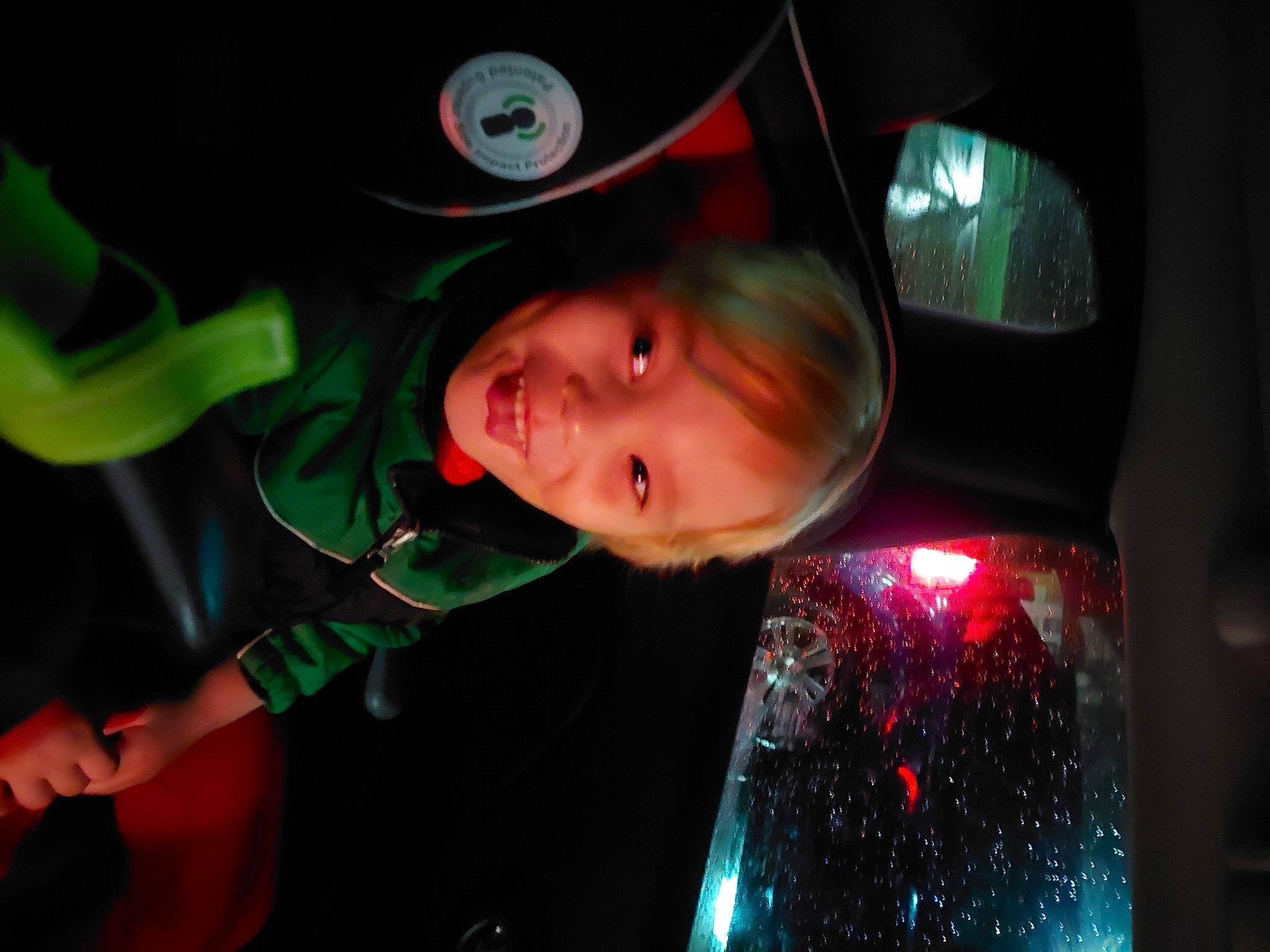 Logan is registered to the contest to win money with this photo: auto_part, automotive_design, automotive_exterior, automotive_lighting, automotive_wheel_system, child, darkness, electric_blue, entertainment, event, fun, glass, hat, joy, luxury_vehicle, magenta, person, smile, toddler, tree