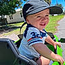 Karson joined the competition — help win amazing prizes! child, toddler, smiling, outdoor, portrait, baseball_cap, short_hair, blue_shirt, numbered_shirt, ride_on_vehicle, toy_vehicle, green_vehicle, steering_wheel, sunlight, grass, palm_trees, house, sidewalk, summer, happy