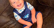 Karson is registered to the contest to win money with this photo: baby, bare_feet, blond_hair, blue_eyes, casual_clothing, child, couch, furniture, happy, home, indoors, infant, leather, overalls, photography, portrait, shark_pattern, shirt, sitting, smiling