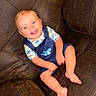 Karson is registered to the contest to win money with this photo: baby, child, smiling, happy, sitting, couch, leather, overalls, shark_pattern, shirt, bare_feet, portrait, indoors, home, furniture, blond_hair, blue_eyes, infant, casual_clothing, photography