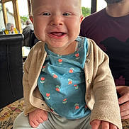 Maisie joined the competition — help win amazing prizes! baby, child, smile, indoor, person, adult, cardigan, blue_shirt, patterned_surface, window, beard, happy, seated, fingers, face, light, casual_clothing, background_people, table, home
