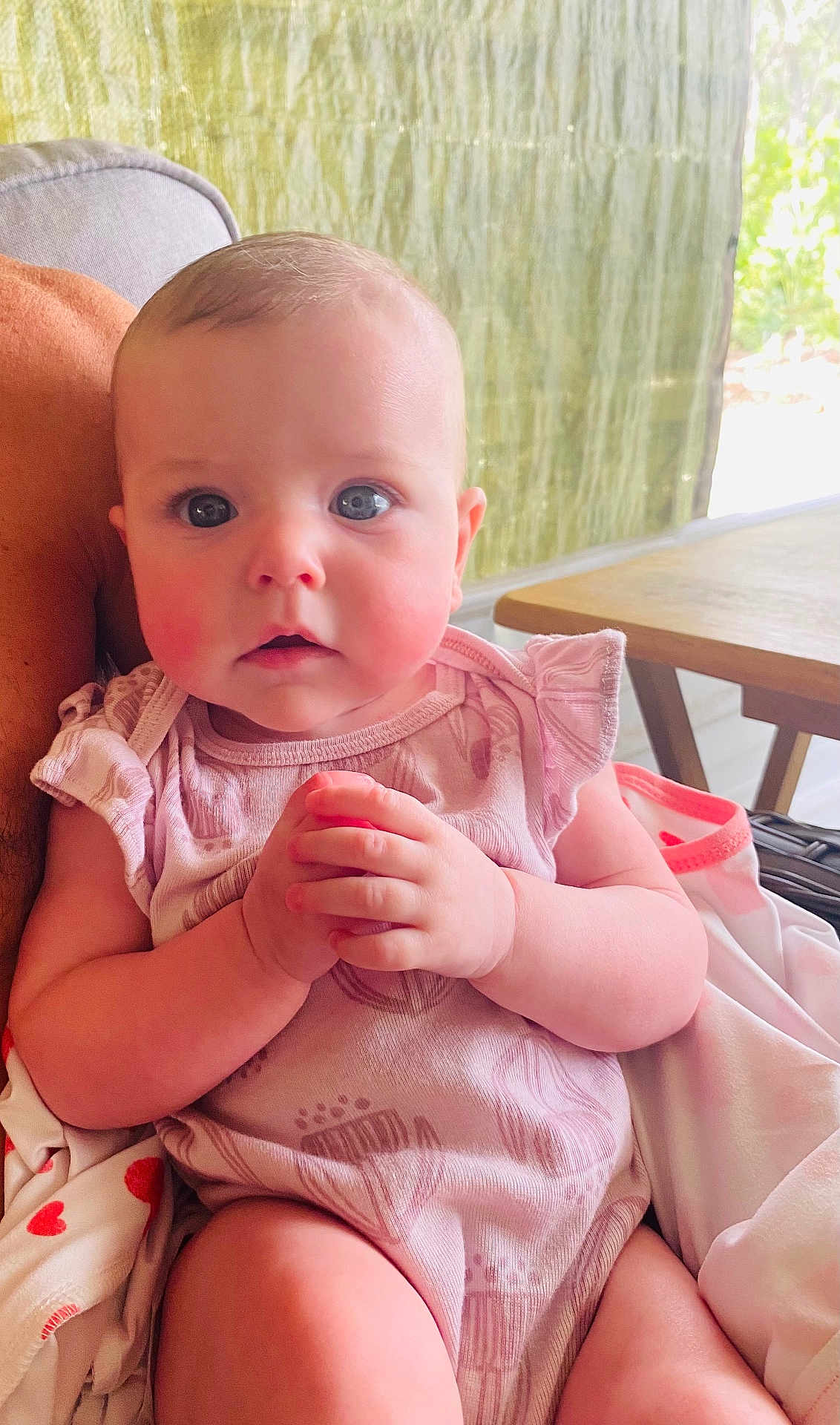 Oakley is registered to the contest to win money with this photo: baby, infant, child, hands, pink_clothing, blue_eyes, rosy_cheeks, blanket, soft_fabric, indoor, seated, curious_expression, cute, portrait, closeup, person, skin, head, face, young