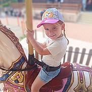 Ambre participe au concours pour gagner de l'argent avec cette photo : child, smiling, carousel, horse, cap, shorts, amusement_park, ride, playful, outdoor, happy, summer, fun, toy, seatbelt, pole, colorful, daytime, people, background