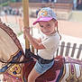 child, smiling, carousel, horse, cap, shorts, amusement_park, ride, playful, outdoor, happy, summer, fun, toy, seatbelt, pole, colorful, daytime, people, background