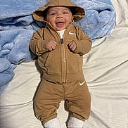 Adriel joined the competition — help win amazing prizes! baby, infant, smiling, hoodie, brown_clothing, nike_logo, white_socks, blanket, bed, striped_sheet, cute, happy, child, young, portrait, indoor, cozy, clothing, person, casual