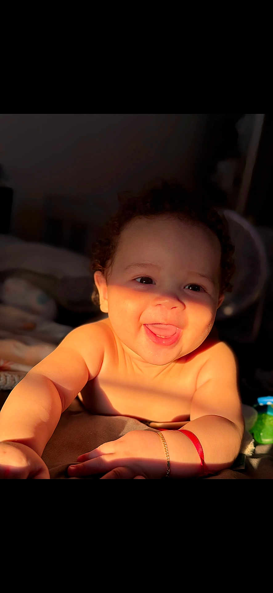 Adriel is registered to the contest to win money with this photo: baby, child, smiling, tongue_out, curly_hair, bracelet, skin, happy, indoors, closeup, face, expression, light, shadow, playful, cute, infant, person, portrait, warm_light
