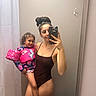 Alaura joined the competition — help win amazing prizes! woman, child, mirror, selfie, bathroom, swimsuit, floatation_vest, unicorn, smile, curly_hair, holding, phone, reflection, curtain, hook, bag, tile_floor, casual, indoor, person