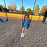 child, girl, swing, playground, park, blue_sky, trees, autumn, grass, gravel, adult, casual_clothing, footwear, dress, sunlight, outdoor, smiling, play, fun, recreation
