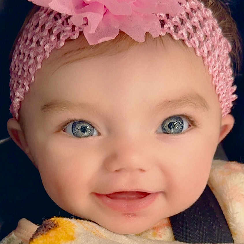Esther is registered to the contest to win money with this photo: baby, infant, smile, face, headband, flower, blue_eyes, blanket, close_up, cute, child, portrait, happy, apparel, soft_texture, indoors, young, warm, headwear, person