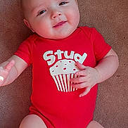 Jaxon is registered to the contest to win money with this photo: baby, infant, onesie, red_onesie, cupcake_graphic, smile, chubby_cheeks, carpet, lying_down, hand, legs, portrait, cute, skin, face, eyes, happy, indoor, clothing, baby_torso