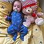 baby, infant, pacifier, plush_toy, teddy_bear, bedspread, yellow, blue_onesie, dinosaur_pattern, sleepwear, child, cute, lying_down, bedroom, soft_toy, striped_hat, bee_pattern, comfort, cozy, nap_time