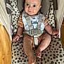 baby, infant, child, seat, straps, bib, clothing, pattern, dots, wood_floor, indoor, person, cute, expression, blue_eyes, skin, foot, hand, fabric, comfort