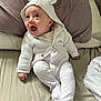 baby, infant, smile, white_clothing, hoodie, knitted, ear_hood, bed, pillow, blanket, happy, cute, child, footed_pajamas, person, indoors, lying_down, expression, young, cozy