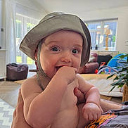 Taylor joined the competition — help win amazing prizes! baby, child, hat, hand, indoor, person, skin, face, diaper, furniture, plant, light, window, curtain, couch, arm, smile, living_room, cheek, holding