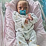 baby, infant, pacifier, crib, blanket, pink, white_clothing, onesie, face, newborn, sleeping_area, soft_toy_pattern, hospital_bassinet, hand, footed_pajamas, cute, child, person, indoor, resting