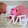 baby, newborn, sleeping, pink_tutu, white_clothing, love_sign, blanket, soft_texture, cute, infant, peaceful, resting, indoors, portrait, closeup, tulle_skirt, decorative_letters, sleep, tiny_feet, cozy