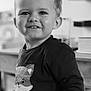 child, toddler, smiling, indoor, black_and_white, face, cute, clothing, fox_graphic, shirt, person, portrait, happy, young, hair, eyes, furniture, background, blurred, standing