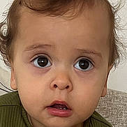 Deniz joined the competition — help win amazing prizes! toddler, child, face, curly_hair, wide_eyes, green_shirt, ribbed_clothing, buttons, indoor, couch, expression, portrait, young_child, casual_wear, curiosity, closeup, person, head_and_shoulders, sitting, innocence