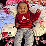 Santi is registered to the contest to win money with this photo: baby, infant, smiling, tongue_out, red_bib, headband, floral_pillow, blanket, blue_blanket, gray_leggings, socks, bed, indoor, cozy, happy, portrait, closeup, soft_fabrics, floral_pattern, cute