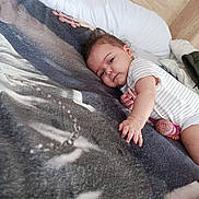 Amaya participe au concours pour gagner de l'argent avec cette photo : baby, infant, bed, blanket, animal_print, striped_clothing, hand, face, wooden_wall, cozy, indoor, resting, curious, soft_texture, plush_toy, cushion, child, person, sleepwear, relaxed