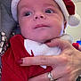 baby, child, santa_hat, red_clothing, hand, rings, nails, face, portrait, holiday, festive, cute, closeup, person, skin, christmas, warm, indoor, adult_hand, costume