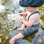 Reid joined the competition — help win amazing prizes! baby, child, water, stream, rocks, hat, blue_cap, suspenders, barefoot, outdoor, nature, curious, sitting, exploring, summer, sunlight, reflection, skin, legs, hands