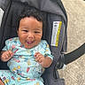 Asiyah is registered to the contest to win money with this photo: baby, child, car_seat, smiling, curly_hair, outdoor, grass, concrete, clothing, happy, person, infant, cute, playful, seat, foot, tongue_out, summer, sunny, colorful