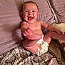 baby, child, diaper, smiling, laughing, indoor, bedspread, pillow, patterned, cute, happy, infant, skin, barefoot, playful, wood_paneling, person, seated, young, expression