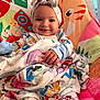 baby, child, smiling, pajamas, head_wrap, colorful, disney, blanket, patterned, chair, animal_print, indoor, cute, happy, portrait, infant, comfort, cushion, playful, cozy