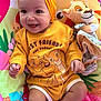 baby, child, smiling, yellow_headband, yellow_clothing, lion_king, plush_toy, play_mat, colorful_background, happy, infant, cute, portrait, indoors, sitting, toy, headband, person, young_child, bright_colors