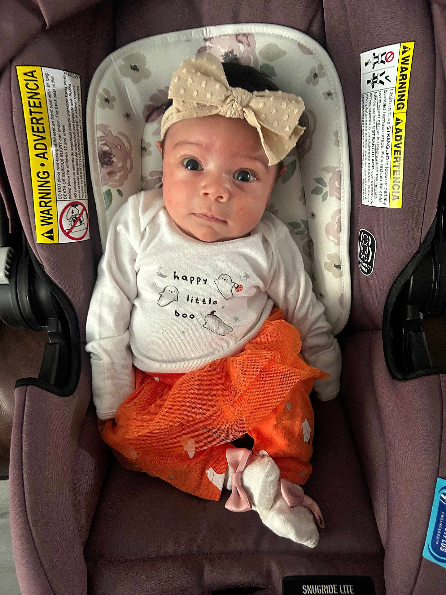 Laylin is registered to the contest to win money with this photo: baby, infant, child, car_seat, headband, bow, tutu, orange, white_shirt, ghosts, happy_little_boo, cute, portrait, indoor, clothing, socks, pink_bow, floral_pattern, purple, seat