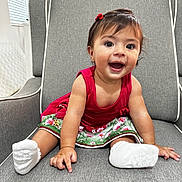 Rebecca is registered to the contest to win money with this photo: baby, child, smiling, dress, red, socks, hair_bow, chair, cushion, indoor, cute, happy, person, portrait, skin, furniture, young_child, seated, hands, feet