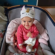 Lyha participe au concours pour gagner de l'argent avec cette photo : baby, unicorn_hat, pink_clothing, soft_toy, baby_seat, cushion, blue_wall, electrical_outlet, smile, cheerful, indoors, child, cute, plush, infant, toy, face, headwear, sitting, cozy
