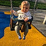 child, toddler, baby, swing, playground, park, chains, seat, socks, striped_socks, smile, face, hair, sunlight, shadow, safety_seat, rubber_surface, fence, outdoor, casual_clothing