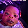 Noah is registered to the contest to win money with this photo: baby, infant, face, close_up, purple_lighting, curly_hair, expression, messy_mouth, clothing, person, indoor, portrait, cute, young_child, skin, head, eyes, nostrils, mouth, newborn