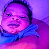 Noah is registered to the contest to win money with this photo: baby, child, face, arm, purple_light, closeup, person, indoor, curly_hair, expression, skin, blue_clothing, portrait, infant, cute, young, head, selfie, funny_face, lighting