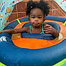 child, toddler, inflatable, pool, water, float, swimming, toy, dinosaur, canopy, blue, orange, green, hair_bow, curly_hair, face, summer, outdoor, water_toy, baby_swimming