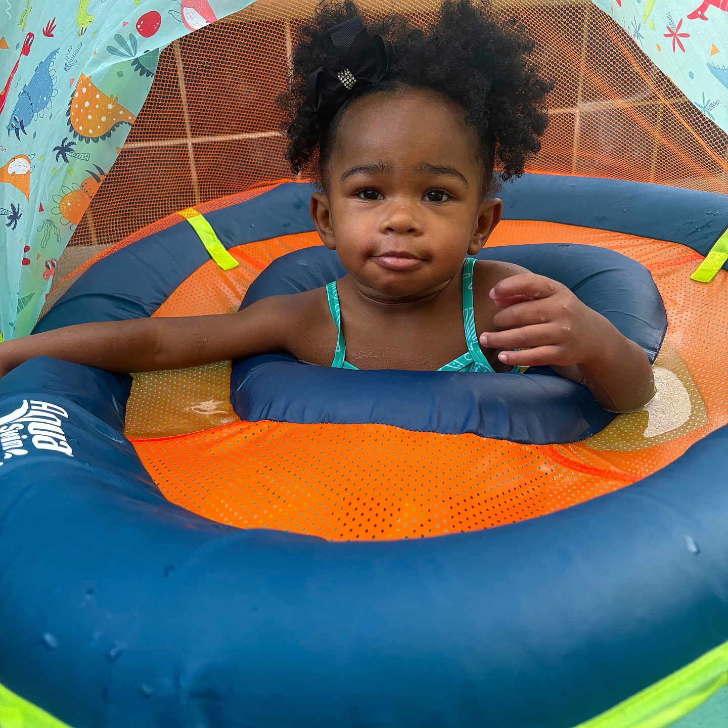 Melody is registered to the contest to win money with this photo: child, toddler, inflatable, pool, water, float, swimming, toy, dinosaur, canopy, blue, orange, green, hair_bow, curly_hair, face, summer, outdoor, water_toy, baby_swimming