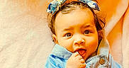 Olive is registered to the contest to win money with this photo: baby, infant, child, blue_bows, blue_clothing, curly_hair, blanket, soft_texture, indoor, portrait, cute, exploring, hands, face, eyes, mouth, button, expression, lying_down, person