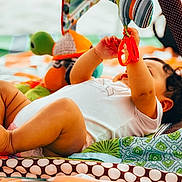 Olive joined the competition — help win amazing prizes! baby, infant, child, playmat, toy, turtle, colorful, patterned, curly_hair, reaching, lying_down, soft_toys, indoor, close_up, cute, chubby, white_clothing, playtime, focus, bright