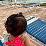 Olive joined the competition — help win amazing prizes! toddler, curly_hair, ponytail, swimsuit, bow, child, outdoor, lounge_chair, poolside, waterfront, water, buildings, paved_ground, hand, person, summer, vacation, relaxation, back_view, colorful_clothing